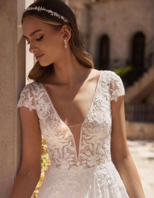 Robes de mariées  Bianco Evento "Agate" est une robe de mariée trapèze, fabriquée avec de la mousseline et de la dentelle de haute qualité. Cette robe de mariée moderne est dotée de manches à godets, d'un décolleté en V sensuel sur le devant et d'un dos ouvert. 