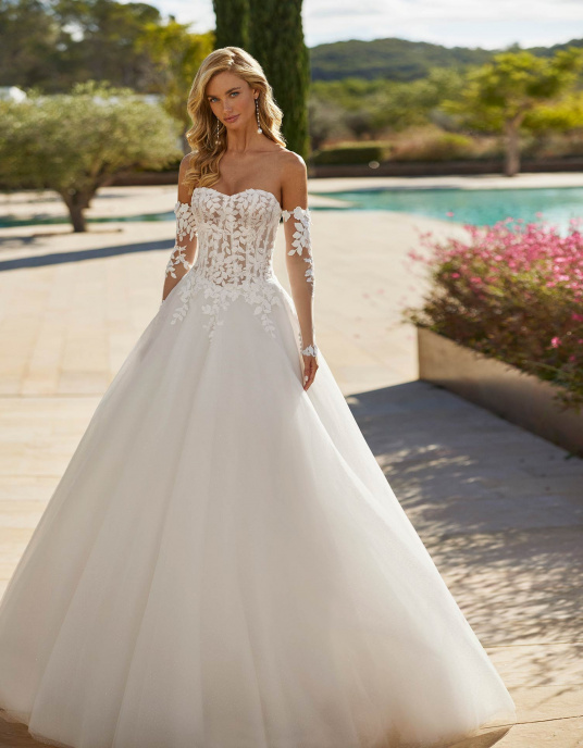 Robes de mariées  ADRIANA ALIER SIMONA est une Robe de mariée longue volumineuse en tulle avec bustier en dentelle, perles, encolure bustier, manches amovibles et dos corset. 