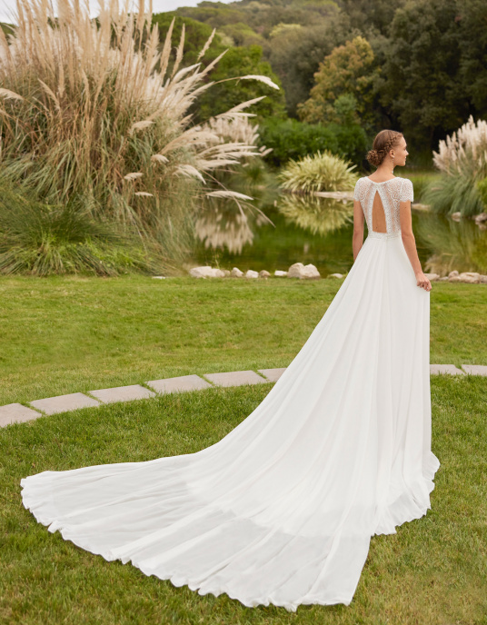Robes de mariées  ADRIANA ALIER RAY Robe romantique style princesse en georgette avec traîne amovible. Elle présente un décolleté plongeant, un dos nu et des manches courtes. Modèle Alma Novia, réalisé en dentelle et georgette. 