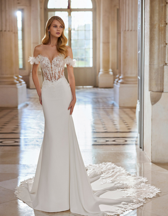 Robes de mariées  ROSA CLARA ELEDIE : Robe de mariée, longue, de coupe sirène et style sexy avec un corsage en dentelle et crêpe. Elle est dotée d’un décolleté illusion, d’un dos boutonné, de bretelles tombantes et d’une fleur d’ornement qui s’harmonise parfaitement avec la dentelle  