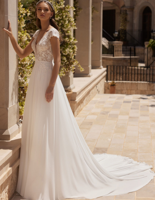 Robes de mariées  Bianco Evento "Agate" est une robe de mariée trapèze, fabriquée avec de la mousseline et de la dentelle de haute qualité. Cette robe de mariée moderne est dotée de manches à godets, d'un décolleté en V sensuel sur le devant et d'un dos ouvert. 
