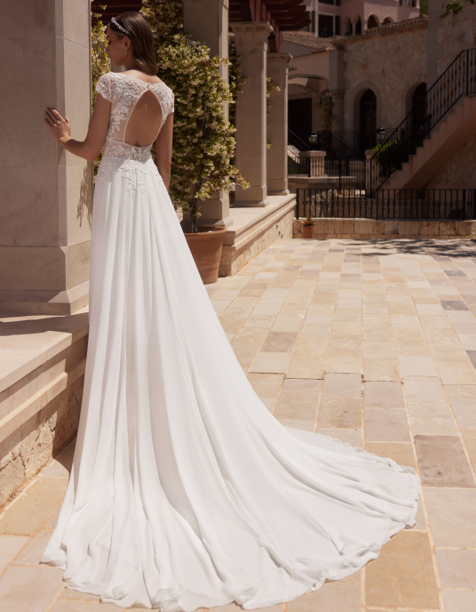Robes de mariées  Nicole Couture "Agate" est une robe de mariée trapèze, fabriquée avec de la mousseline et de la dentelle de haute qualité. Cette robe de mariée moderne est dotée de manches à godets, d'un décolleté en V sensuel sur le devant et d'un dos ouvert. 