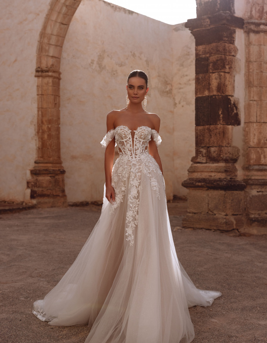 Robes de mariées  Nicole Couture Ariella allie glamour et romance moderne. Son corset structuré et ses manches délicates soulignent la silhouette, tandis que la jupe en tulle léger flotte avec élégance. Les appliqués de dentelle ajoutent raffinement et profondeur.  