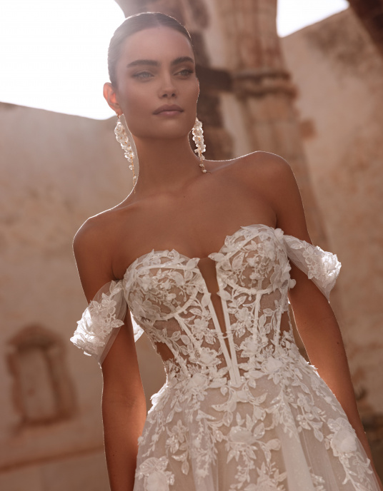 Robes de mariées  Nicole Couture Ariella allie glamour et romance moderne. Son corset structuré et ses manches délicates soulignent la silhouette, tandis que la jupe en tulle léger flotte avec élégance. Les appliqués de dentelle ajoutent raffinement et profondeur.  