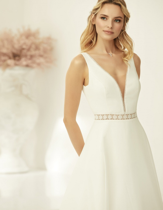 Robes de mariées  Bianco Evento AZARIA : Azaria, robe de mariée moderne en mousseline de haute qualité, avec jupe droite et traîne élégante. Décolleté en V plongeant bordé de dentelle et voilage en tulle discret au centre. Dos en V plongeant, taille soulignée par une délicate dentelle a 