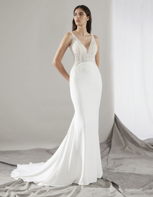Robes de mariées  Pronovias CLIN coupe sirène est une ode à votre silhouette, avec son corsage décolleté en V et ses bretelles brodées. La dentelle brodée de paillettes orne votre taille avec une subtile transparence. Le dos nu présente un décolleté en V plongeant. 