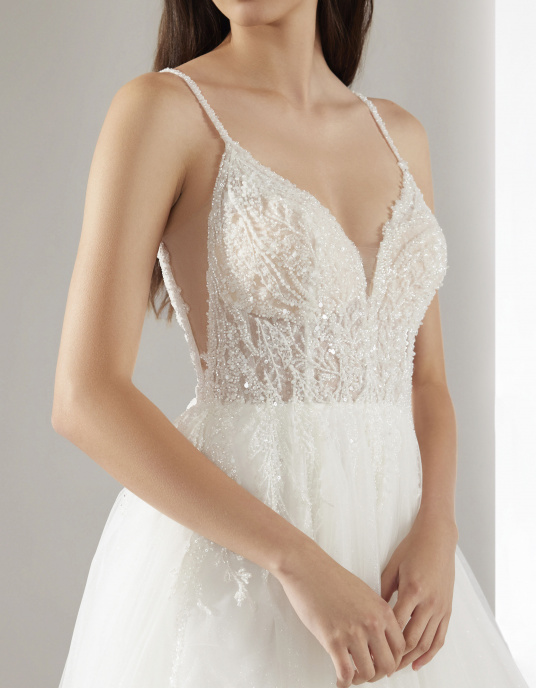 Robes de mariées  Pronovias HERO-Le corsage, décolleté en V avec des bretelles ornées de bijoux et confectionné en dentelle très fine brodée de paillettes, glisse sur la jupe en tulle dans un jeu de transparences. 