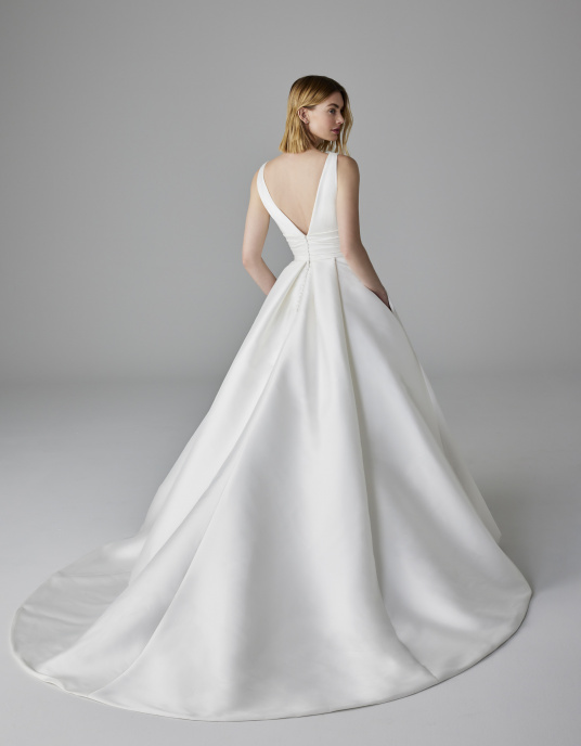 Robes de mariées  Pronovias LUMINEUSE-Cette robe en mikado présente des fentes en V sur le décolleté, sur les côtés et dans le dos, une ceinture large plissée et une superbe jupe princesse texturée ornée de poches pratiques. 