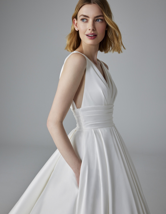 Robes de mariées  Pronovias LUMINEUSE-Cette robe en mikado présente des fentes en V sur le décolleté, sur les côtés et dans le dos, une ceinture large plissée et une superbe jupe princesse texturée ornée de poches pratiques. 