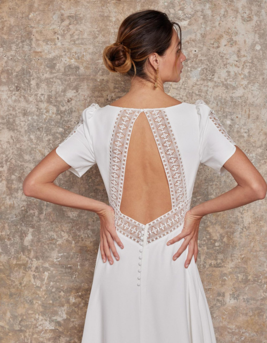 Robes de mariées  Lambert Creation Lys Allure chic et couture pour cette robe originale avec ses manches courtes incrustées de guipure sa ceinture en transparence et son dos bordé de guipure. 