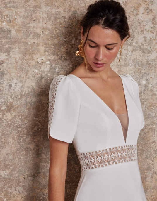 Robes de mariées  Lambert Creation Lys Allure chic et couture pour cette robe originale avec ses manches courtes incrustées de guipure sa ceinture en transparence et son dos bordé de guipure. 