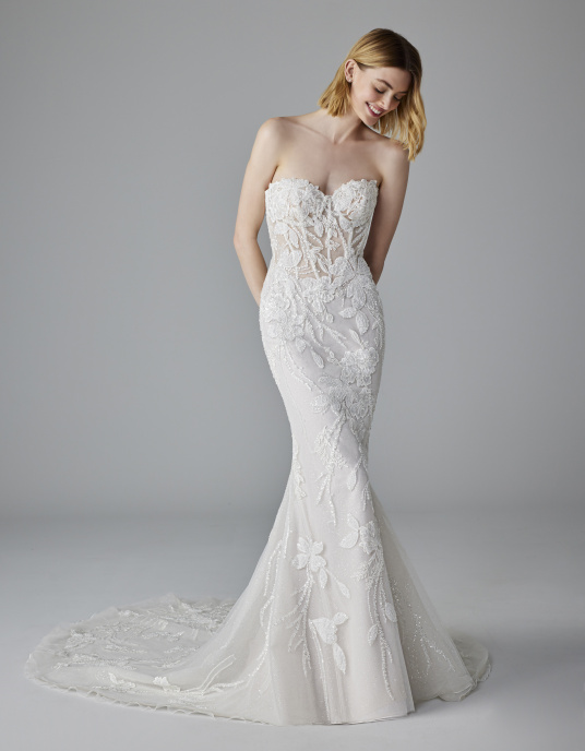 Robes de mariées  Pronovias NUAGE-un corsage renforcé style corset et une jupe seyante qui épouse la silhouette jusqu’aux genoux puis s’évase pour former une traîne sophistiquée. La dentelle et les strass créent des motifs et des formes qui font de ce modèle une véritable œuvre d’ar 