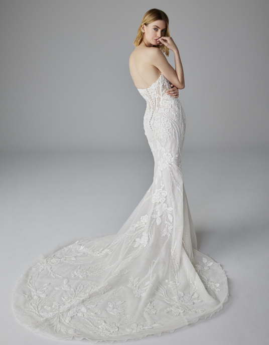 Robes de mariées  Pronovias NUAGE-un corsage renforcé style corset et une jupe seyante qui épouse la silhouette jusqu’aux genoux puis s’évase pour former une traîne sophistiquée. La dentelle et les strass créent des motifs et des formes qui font de ce modèle une véritable œuvre d’ar 